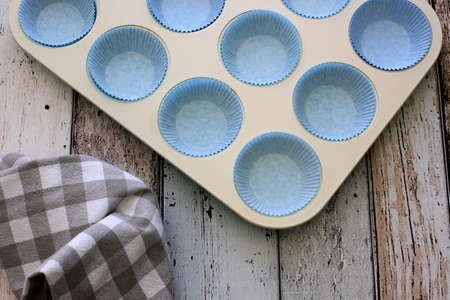 Empty baking pan for cupcakes with brown kitchen towel on wooden table