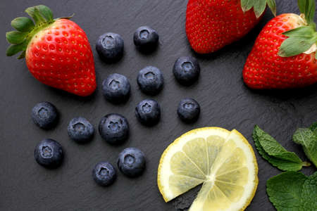 Strawberries, group of blueberries, lemon slices and some mint leaves on slate backgroundの写真素材