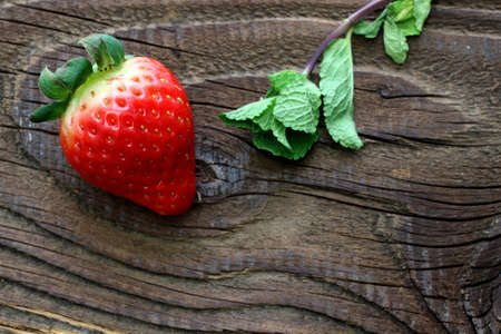 Single strawberry with mint leaves on antique tableの写真素材