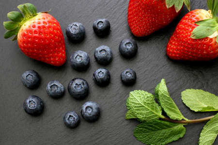 Strawberries, group of blueberries and some mint leaves on slate backgroundの写真素材