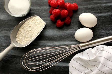 Baking ingredients sugar, flour, eggs and group of raspberries with shawls on white and black...