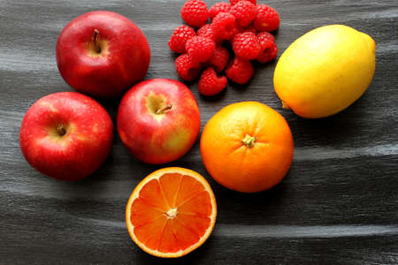 Apple, group of raspberries, orange and lemon on shabby, black and blue board, top viewの写真素材