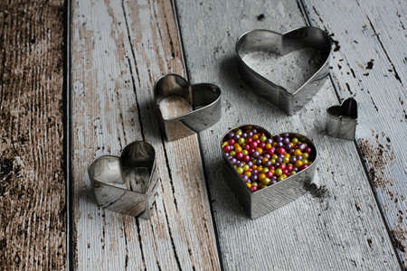 Heart shape pastry cutter with colorful sugar pearls on wooden table