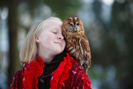 Cute girl in red scarf standing with little owl in a parkの写真素材