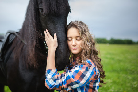 Young beautiful girl with frisian horse standing in the meadow at summer timeの写真素材