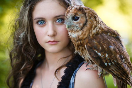 Portrait of beautiful young girl with owl in a forest at summer timeの写真素材