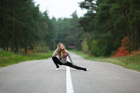 Young professional gymnast makes splits on the road at autumn time