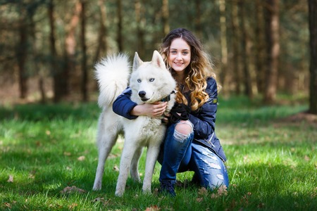 Happy young girl embracing husky dog in a forest at spring time