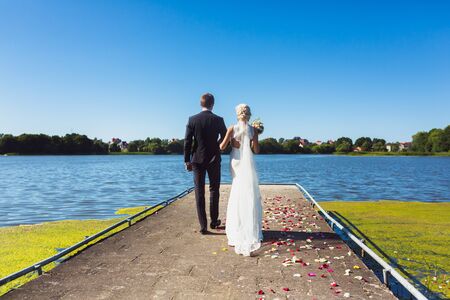 Happy wedding couple walking on embankment of riverの写真素材