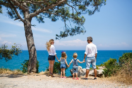Happy family with two kids standing on the seacoast near pine treeの写真素材