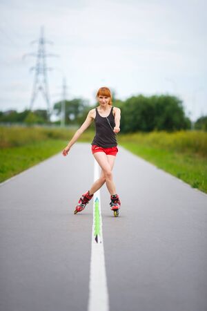 Attractive young girl rollerblading on the road at summer time