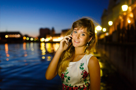 Pretty young girl talks on mobile phone in the night cityの写真素材