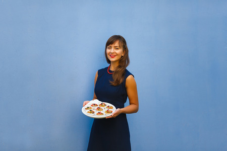 Young woman holding a tray with cupcakes on the blue background outdoorの写真素材