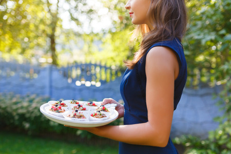 Young woman holding a tray with cupcakes in the gardenの写真素材