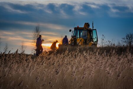 Group of workers near the tractor at evening timeの写真素材