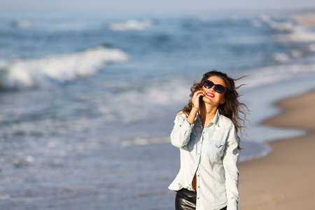 Woman talking by the phone on the beach at autumn timeの写真素材