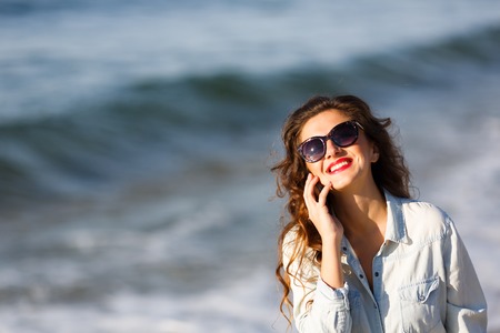 Woman talking by the phone on the beach at autumn timeの写真素材