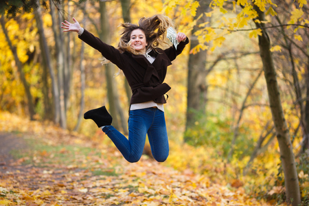 Happy young smiling girl jump with the several one hundred dollars' banknotes in the hand on the yellow backgroundの写真素材