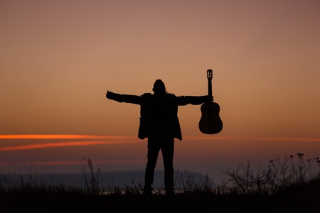 Man standing with guitar in sunset timeの写真素材