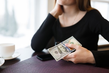 Young woman holding a one hundred dollar bill sitting in a cafe waiting for the waiterの写真素材
