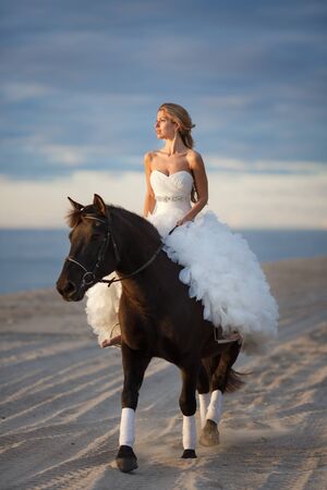 Bride riding a horse on the beach at sunsetの写真素材