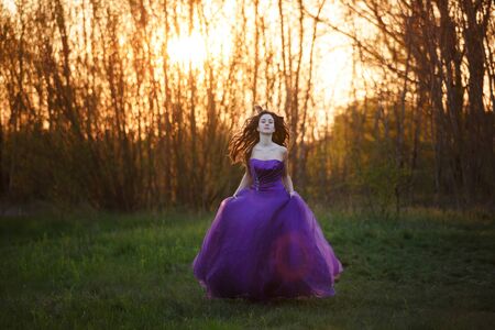 Running attractive girl dressed evening gown at sunsetの写真素材