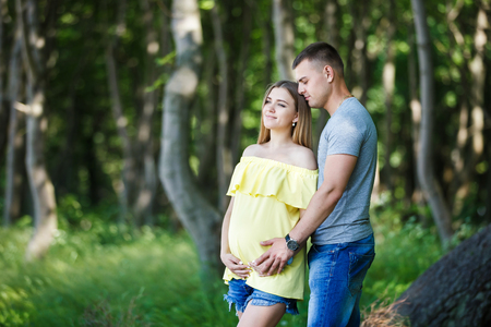 Hugging young pregnant couple standing in a forest