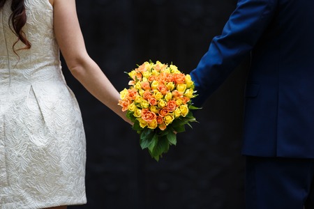 Hands of newlyweds holding the bridal bouquet on a black backgroundの写真素材