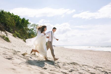 Cheerful wedding couple running on the beach at summer timeの写真素材