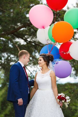 Young wedding couple with colored balloons hugging in the pine forestの写真素材
