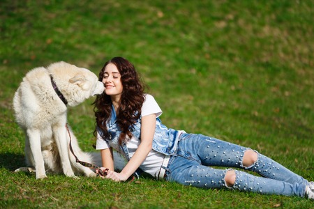 White husky is sniffing at young girl, lying on the grass