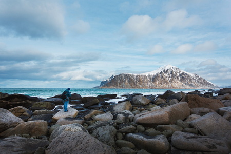 The photographer is shooting the high wave on a stony coast in the background of a snowy mountain in the Lofoten Islandsの写真素材