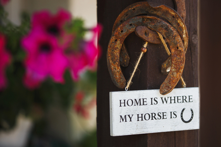Sign of HOME IS WHERE MY HORSE is hanging on the rusty horseshoes on a wooden pole on a background of flowersの写真素材