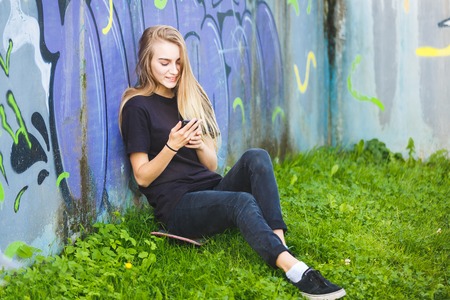 Young female skateboarder with smartphone in her hand against the background of graffiti wallの写真素材