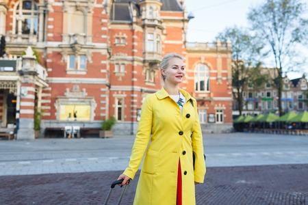 The woman with suitcase is walking in the street of Amsterdam city in autumnの写真素材