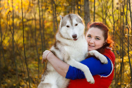 The dog breeder is hugging with her husky dog in autumn forestの写真素材