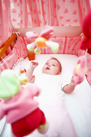Little happy infant in a pink bed with toysの写真素材