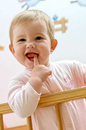 Smiling baby standing in a wood pink bedの写真素材