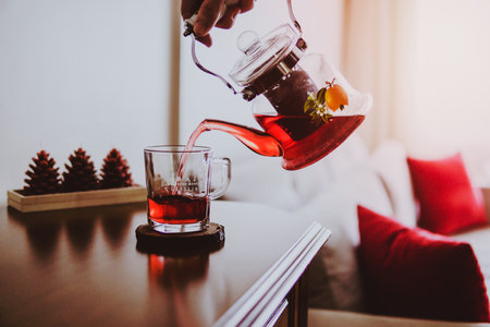 A person pouring tea from a teapot into a glass on a wooden coaster.の写真素材
