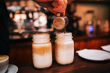 A person pouring coffee into jars with foamed milk.の写真素材
