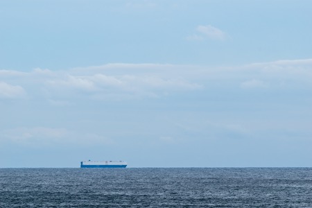 Cargo ship on calm water crossing the horizon on a beautiful sunny dayの写真素材
