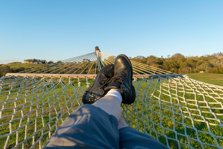Man with black boots relaxing in a hammock in a green field on a beautiful day