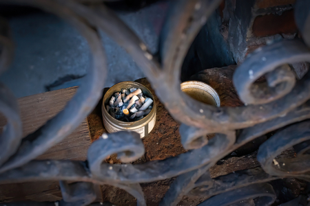 Discarded cigarette butts in a makeshift ashtray left by an open cellar window