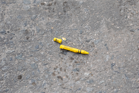 Broken yellow crayon lying on a dirty gray concrete streetの写真素材