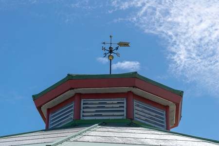 A weather vane atop an old building against a blue sky with some light fluffy cloudsの写真素材
