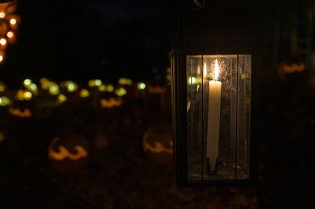 Old-fashioned, candle-lit lantern, with carved and illuminated Halloween pumpkins in the background