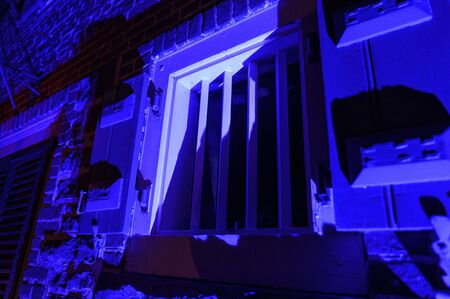 Old-fashioned window with strong metal bars at night, illuminated in blue