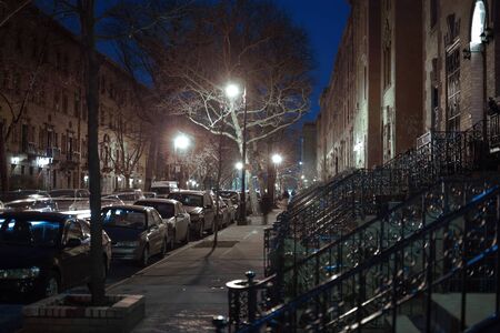 Nighttime shot, looking down a small street, with street lamps trees and building facade in Harlem,...