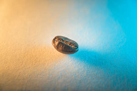 Close-up of a single roasted coffee bean, isolated on an orange and blue colored backgroundの写真素材