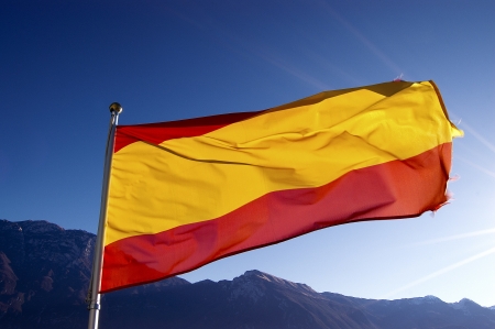 Red and yellow national spanish flag blowing in the wind with blue skyの写真素材